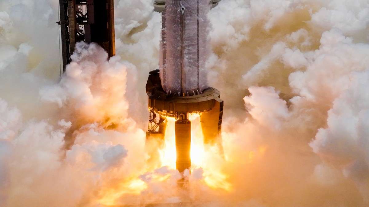 A reusable rocket undergoing static fire test on launch pad, with engines firing but vehicle remaining grounded.